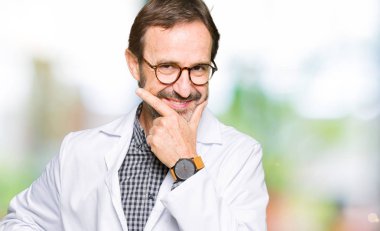 Orta yaş doktor erkek tıbbi giyiyor emin çapraz kollar ve çeneme kaldırdı el ile gülümseme ile kamera seyir ceket. Pozitif düşünce.