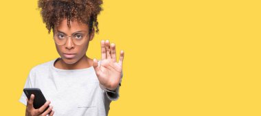 Açık eliyle dur işareti ile ciddi ve kendine güvenen ifade, savunma jest yapıyor izole arka plan üzerinde akıllı telefon kullanan genç Afro-Amerikan kadın
