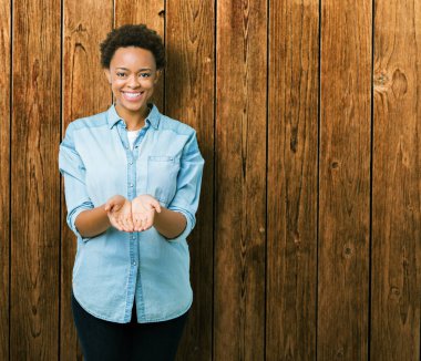 İzole arka plan üzerinde genç güzel bir Afrikalı-Amerikalı kadın gülen ellerle birlikte alma veya jest vererek palms. Ayrı tutma ve koruma