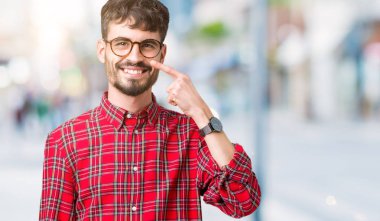 Genç yakışıklı adam gözlük izole üzerinde işaretleme için yüz ve burun, neşeli gülümseyerek el parmak ile arka plan