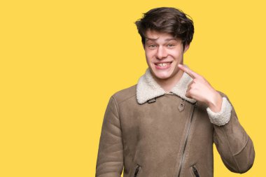 İzole arka plan üzerinde kış ceket giyen genç yakışıklı adam yüz ve burun, neşeli gülümseyen el parmak ile Işaret