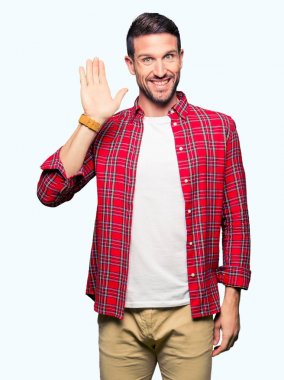 Yakışıklı adam rahat gömlek Waiving selam söyleyerek mutlu ve gülümseyerek giyiyor, dostça karşılama jest