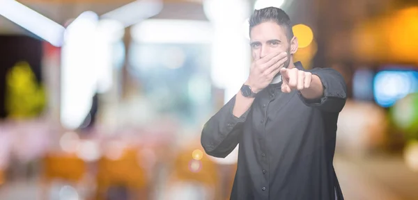 Young Christian priest over isolated background Laughing of you, pointing to the camera with finger hand over mouth, shame expression