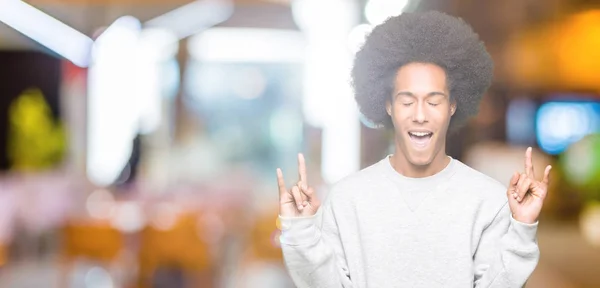 年轻的非洲裔美国男子穿着运动运动衫 用疯狂的表情大喊大叫 用双手做摇滚符号 音乐明星重概念 — 图库照片