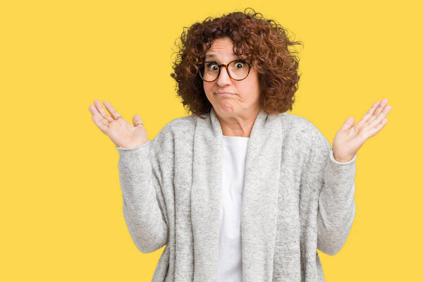 Beautiful middle ager senior woman wearing jacket and glasses over isolated background clueless and confused expression with arms and hands raised. Doubt concept.