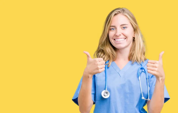 美丽的年轻医生妇女穿着医疗制服在孤立的背景成功标志做积极的手势 竖起大拇指微笑和快乐 带着欢快的表情 获胜者的手势看着镜头 — 图库照片
