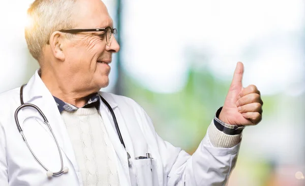 医療コートを着たハンサムな先輩医師男性自慢に見える 横に親指を上げて笑顔 — ストック写真