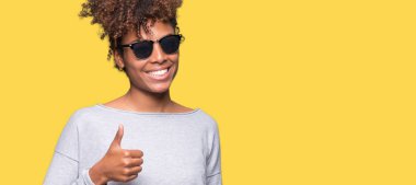 Güzel genç Afro-Amerikan kadın hareketi el ile mutlu yaşasın yapıyor izole arka plan üzerinde güneş gözlüğü takıyor. Kameraya bakarak başarı gösteren ile ifade onaylama.