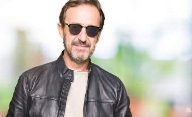 Orta yaş yakışıklı adam yüzünde güneş gözlüğü ve ciddi ifade ile siyah deri ceket giyiyor. Basit ve doğal kameraya bakıyor.