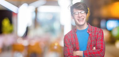 İzole arka plan mutlu yüz ile gülümseyen üzerinde gözlük takan genç yakışıklı öğrenci adam kameraya seyir silah geçti. Olumlu bir kişi.