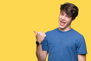 Genç yakışıklı adam izole arka plan üzerinde mavi t-shirt giyen mutlu yüz görünümlü ve başparmak ile yan işaret ile gülümseyen.