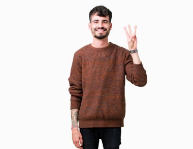 Gösterilen arka plan üzerinde kış kazak giyen genç yakışıklı adam izole ve parmakları ile işaret kendinden emin ve mutlu gülümseyerek iken üçüncü.