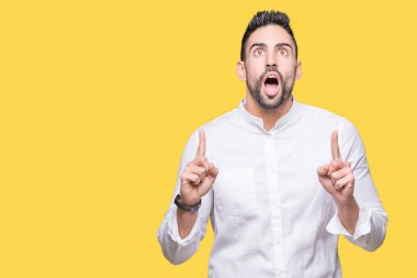 Izole arka plan üzerinde genç iş adamı şaşırttı ve yukarı bakarak ve parmakları ile işaret ve kolları kaldırdı şaşırttı.