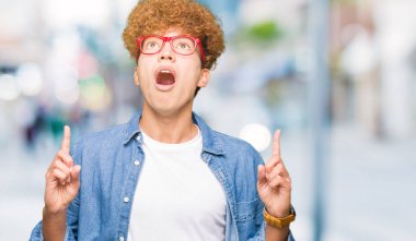 Afro saçlı gözlüklü genç yakışıklı adam hayret ve yukarıya bakıyor ve parmakları ile işaret ve silah kaldırdı şaşırttı.