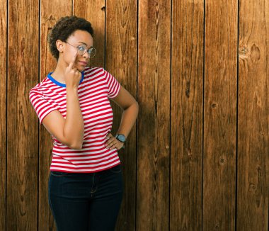 Güzel genç Afro-Amerikan kadın gözlük izole üzerinde arka plan işaret jest göz izlemek için şüpheli ifade