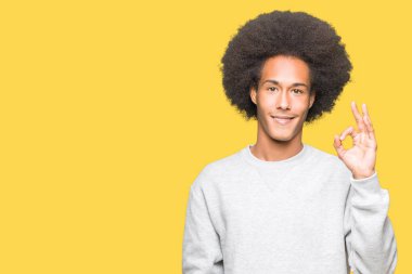 Afro saç giyen sportif kazak el ve parmaklar ok işaretiyle yapıyor olumlu gülümseyen genç Afro-Amerikan adam. Başarılı ifade.