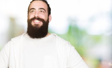 Uzun saçlı ve sakal giyen sportif sweatshirt, yüzünde gülümseme ile yan bakmak, doğal ifade ile genç adam. Güven gülüyor.