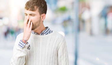 Yakışıklı delikanlı izole arka plan üzerinde kış kazak giyen el ağzıyla kapsayan yorgun esneme sıkılmış. Restless ve uyku hali.