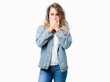 İzole arka plan üzerinde kot ceket giyen güzel genç sarışın kadın hata eller ile ağız kapsayan şok. Gizli konsept.