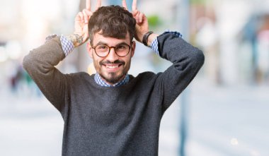 Neşeli gülümseyen izole arka plan tavşan kulakları, komik ve çılgın baş parmaklar ile poz üzerinde gözlük takan genç yakışıklı zeki adam