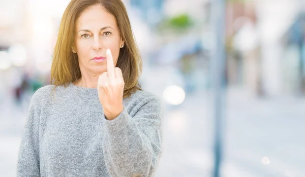 Beautiful middle age woman wearing winter sweater over isolated background Showing middle finger, impolite and rude fuck off expression