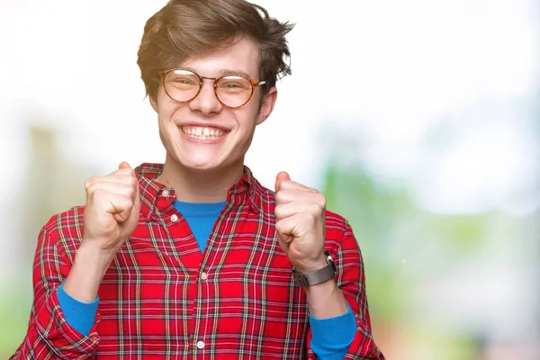 Young handsome man wearing glasses over isolated background excited for success with arms raised celebrating victory smiling. Winner concept.