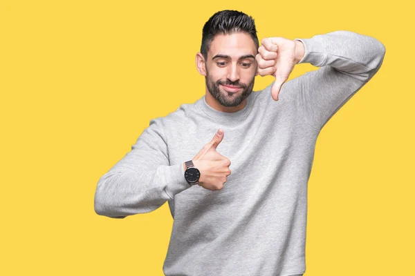 Young handsome man wearing sweatshirt over isolated background Doing thumbs up and down, disagreement and agreement expression. Crazy conflict