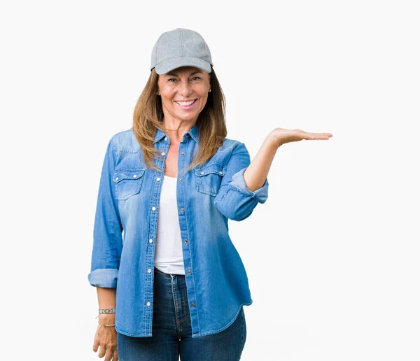陽気な提示とカメラを見て手の手のひらで指している笑みを浮かべて分離の背景にスポーツ キャップを着て美しい中年女性 — ストック写真