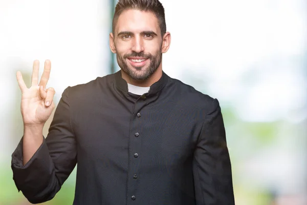 Young Christian priest over isolated background showing and pointing up with fingers number three while smiling confident and happy.