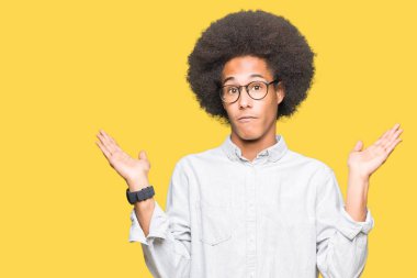 Afrikalı-Amerikalı genç afro saçlı gözlük clueless ve şaşkın bir ifadeyle kollar ve eller kaldırdı giyiyor. Şüphe kavramı.