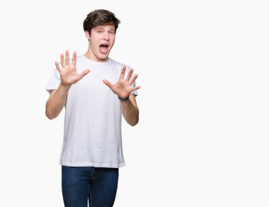Şokta bağırarak korkuyor ve dehşet korku ifade dur hareketi el ile ile izole arka plan üzerinde rahat beyaz t-shirt giyen genç yakışıklı adam. Panik kavramı.