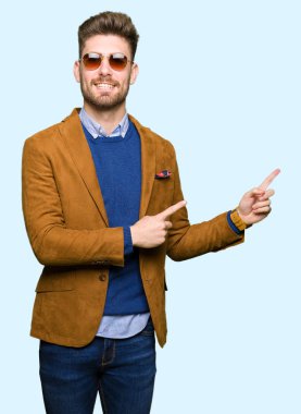 Genç yakışıklı zarif adam gülümseyerek ve iki elleri ve parmakları ile tarafına işaret kamera bakarak güneş gözlüğü takıyor.