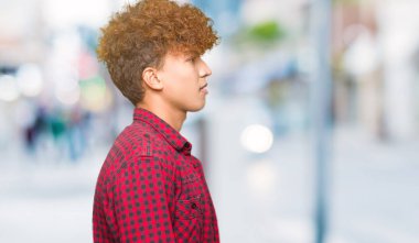 Afro saçlı Genç yakışıklı öğrenci adam yan arayan bir ceket giyiyor, rahat bir gülümseme ile doğal yüzü ile profil poz rahatlayın.