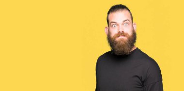 Komik surat ile rahat t-shirt şişirme yanakları giyen genç sarışın adam. Ağız ile hava, deli ifade şişirilmiş.