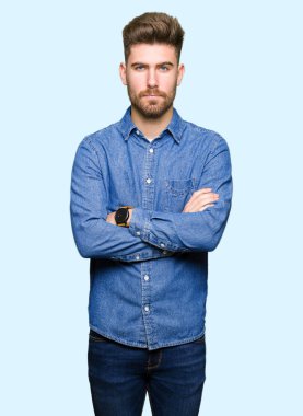 Yüz çapraz silah ile rahat kot gömlek şüpheci ve sinir, onaylamayan ifade giyen genç yakışıklı sarışın adam. Negatif kişi.