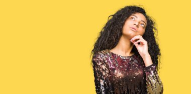 Kıvırcık saçlı giyen gece parti ile genç güzel kız elbise çene düşünme hakkında soru, dalgın ifade üzerine el ile. Düşünceli yüzüyle gülümsüyor. Şüphe kavramı.