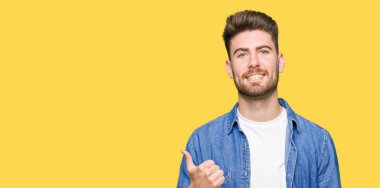 Rahat denim ceket giyen genç yakışıklı sarışın adam el ile jest kadar mutlu başparmak yapıyor. Başarı göstererek kameraya bakarak ifadeyi onaylama.