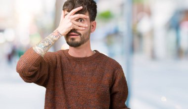 Mahcup ifadeyle parmaklarımın arasından seyir yüz ve gözler el ile kapsayan şok bakmak izole arka plan üzerinde kış kazak giyen genç yakışıklı adam.