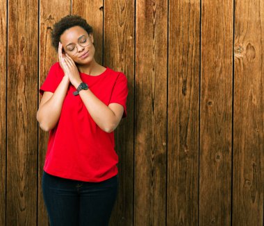 Güzel genç Afro-Amerikan kadın uyku yorgun hayal ve ellerle birlikte poz ile kapalı gözler gülümseyen izole arka plan üzerinde gözlük.