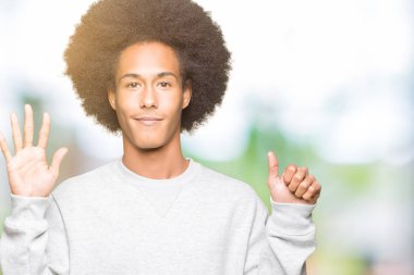 Afro saçlı kadar sportif kazak gösterme ve işaret parmakları ile giyen genç Afro-Amerikan adam kendinden emin ve mutlu gülümseyerek süre 6 numara.