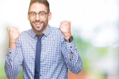 İzole arka plan üzerinde kutluyor gözlük takan genç iş adamı şaşırttı ve başarı için kaldırdı kollarını açarak hayret ve gözleri açık. Kazanan kavramı.