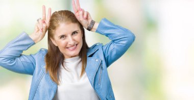 Neşeli gülümseyen komik ve çılgın baş parmaklar ile kulakları, tavşan poz izole arka plan üzerinde moda deri ceket giyen güzel orta yaş Olgun kadın