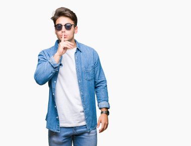 Genç yakışıklı adam dudaklarında parmak ile sessiz olmanı izole arka plan üzerinde güneş gözlüğü takıyor. Sessizlik ve gizli kavramı.