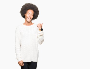 Seyir ve başparmak yanında yukarıyı mutlu yüz ile gülümseyen kış kazak giyen afro saçlı genç Afro-Amerikan adam.