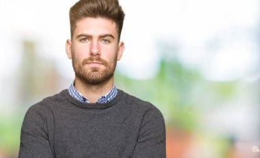 Genç yakışıklı zarif adam şüpheci ve sinir, kesişmiş silah ile yüz ifade onaylamıyor. Negatif kişi.