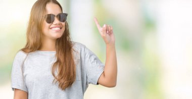 Genç güzel esmer kadın izole arka plan üzerinde güneş gözlüğü giyen başarılı bir fikir parmak yukarı işaret. Çıkıldı ve mutlu. Bir numara.