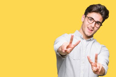 Zafer işareti yapıyor parmak gösterilen kamera seyir gülümseyen izole arka plan üzerinde gözlük takan yakışıklı delikanlı. İki numaralı.