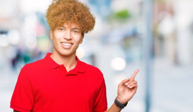 Yüze büyük bir gülümseme ile kırmızı t-shirt giyen afro saç ile genç yakışıklı adam, kamera bakarak yan el ve parmak ile işaret.