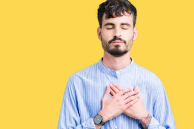 Genç yakışıklı iş adamı izole arka plan ile gülümseyen üzerinde kapalı gözler ve yüzünde minnettar jest ile göğüs üzerinde eller. Sağlık kavramı.