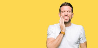 Diş ağrısı veya dişlerde dişlerle ilgili hastalık nedeniyle yakışıklı adam giyiyor rahat beyaz tişört dokunmadan ağız acı ifadesi ile el ile. Diş hekimi kavramı.